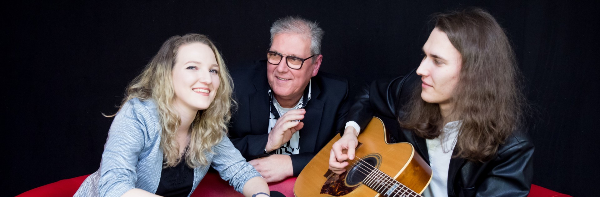 Horst Friedrich mit Tochter Anna und Sohn Lukas und ihren Instrumenten auf beziehungsweise hinter einem roten Sofa. - © The Rich Family