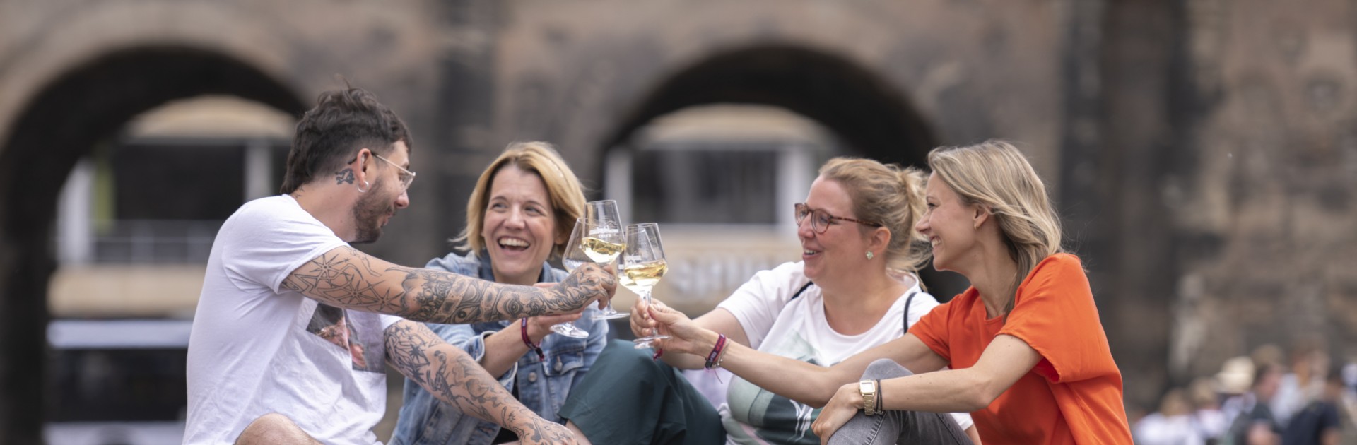 Vier Personen trinken Wein vor der Porta Nigra in Trier - Wein-Rundgang Moselwein trifft Geschichte - © Victor Beusch / Trier Tourismus und Marketing GmbH